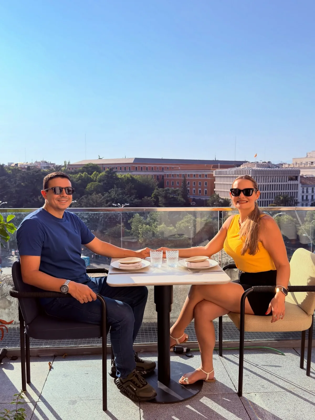 Lore e o marido sentados à mesa de um terraço em Madri, com vista para os prédios da cidade ao entardecer